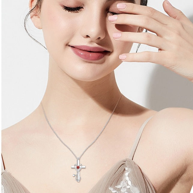 Woman wearing a necklace with a red heart pendant against a plain background